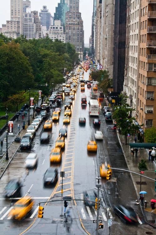 Rainy city avenue with moving traffic, representing market movement after rate cuts