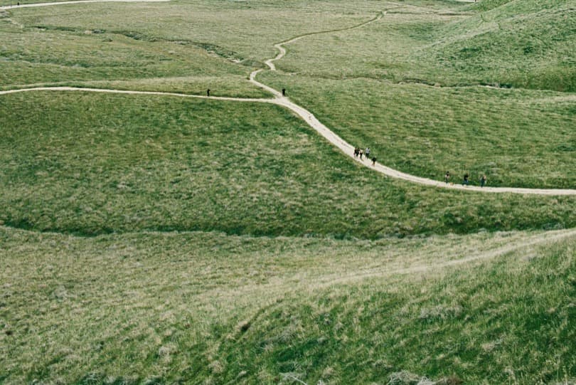 People walking along a winding path through green hills